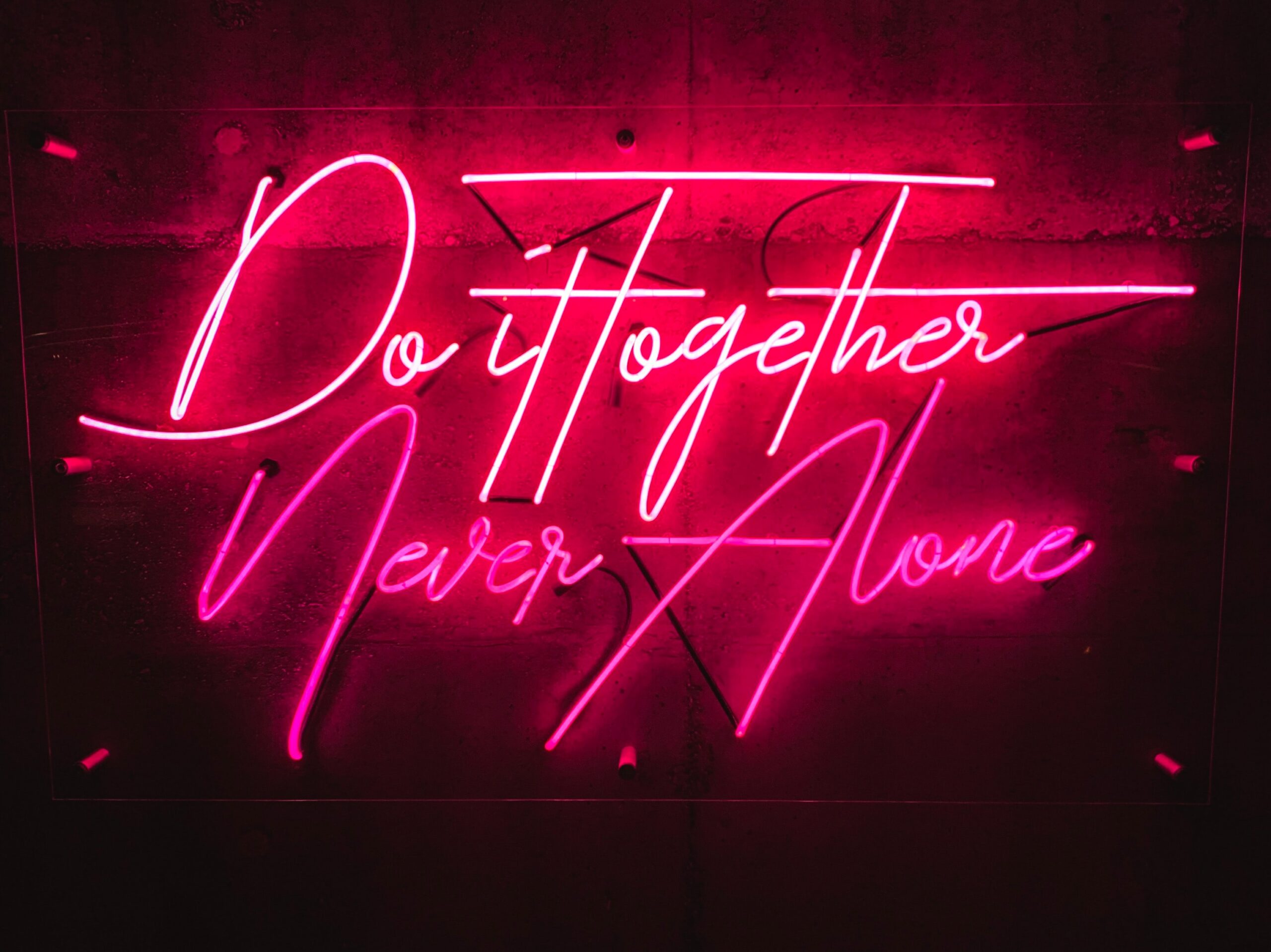 Pink neon on a black background. Text reads, "Do it together, never alone."