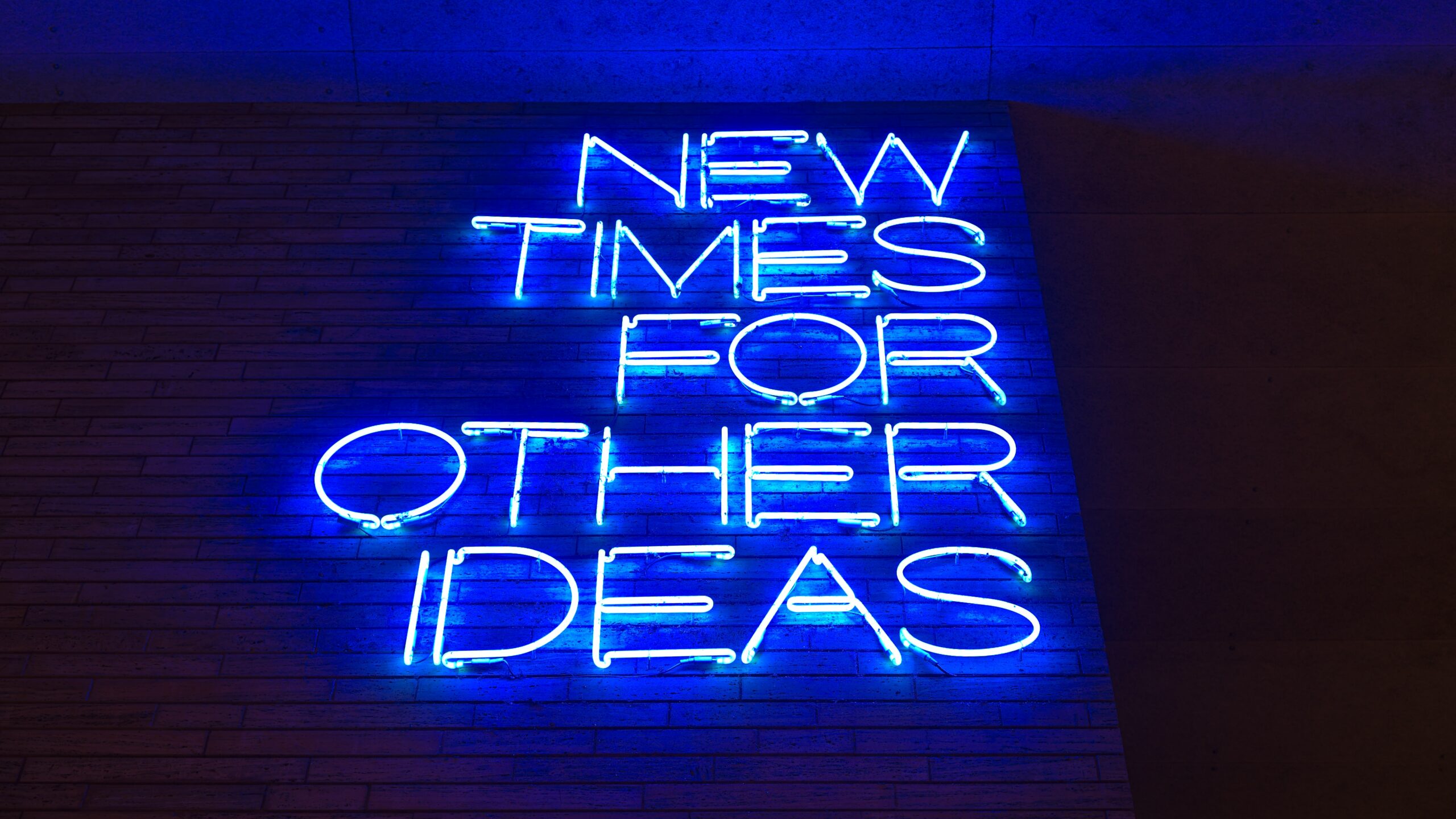 Blue text in neon on a brick wall reads "New times for other ideas." The photo is shot from below.